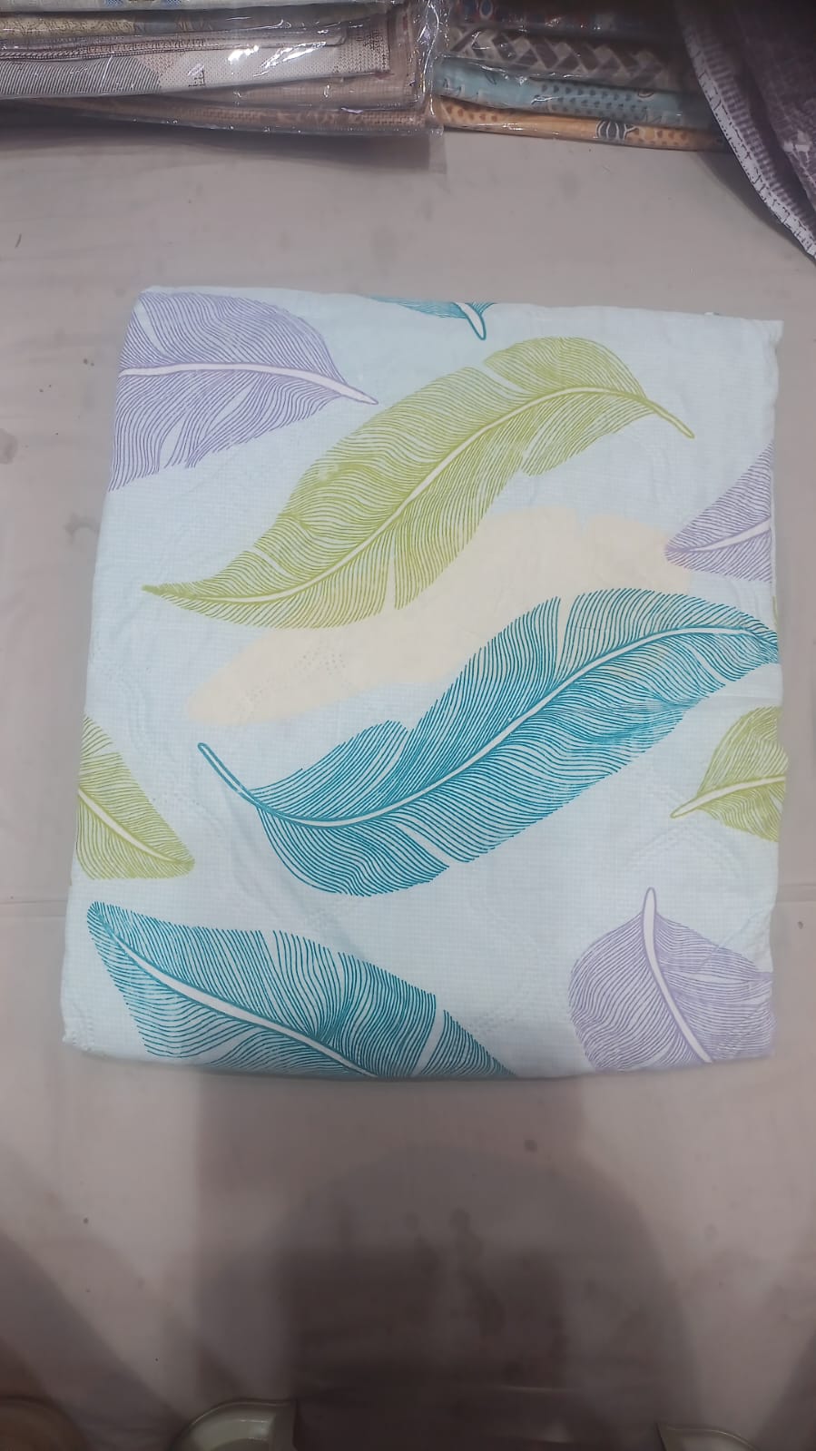 White bedsheet with colourful feather print in teal green and purple